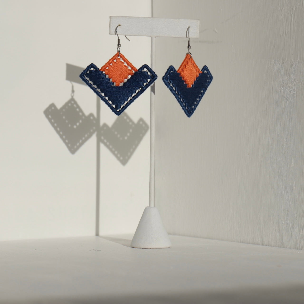 The Baroq earrings in orange and navy blue displayed on a jewelry stand.