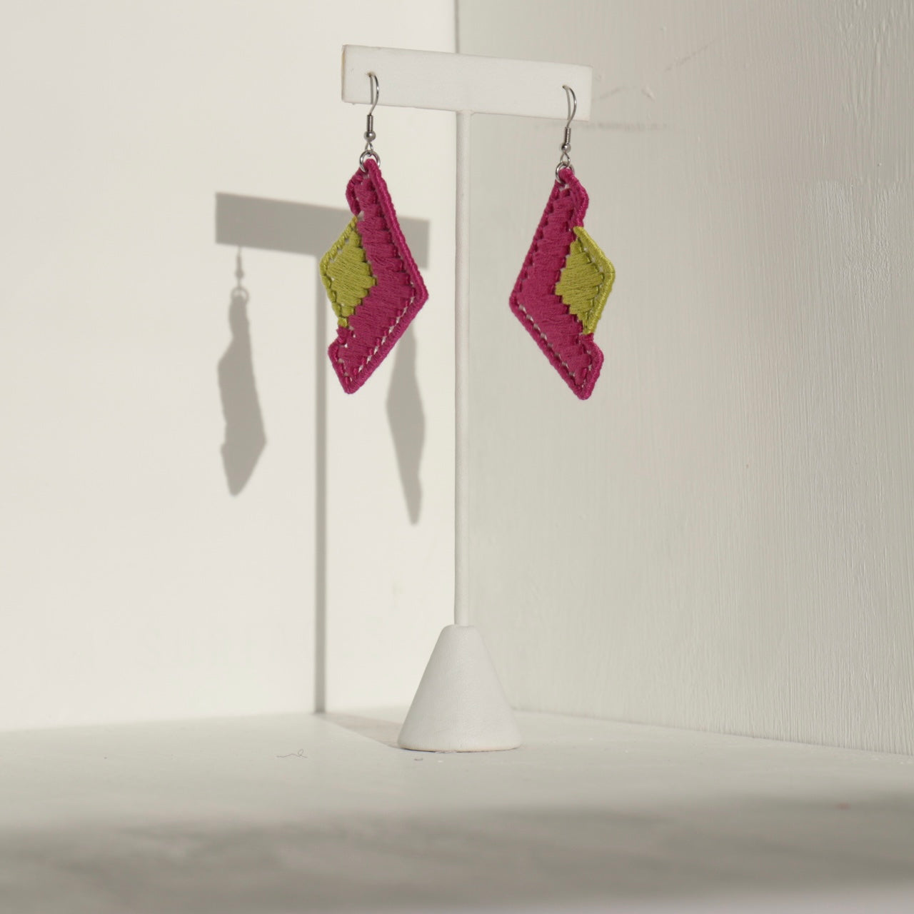 The Baroq statement earrings in pink and green displayed on a jewelry stand with soft lighting.