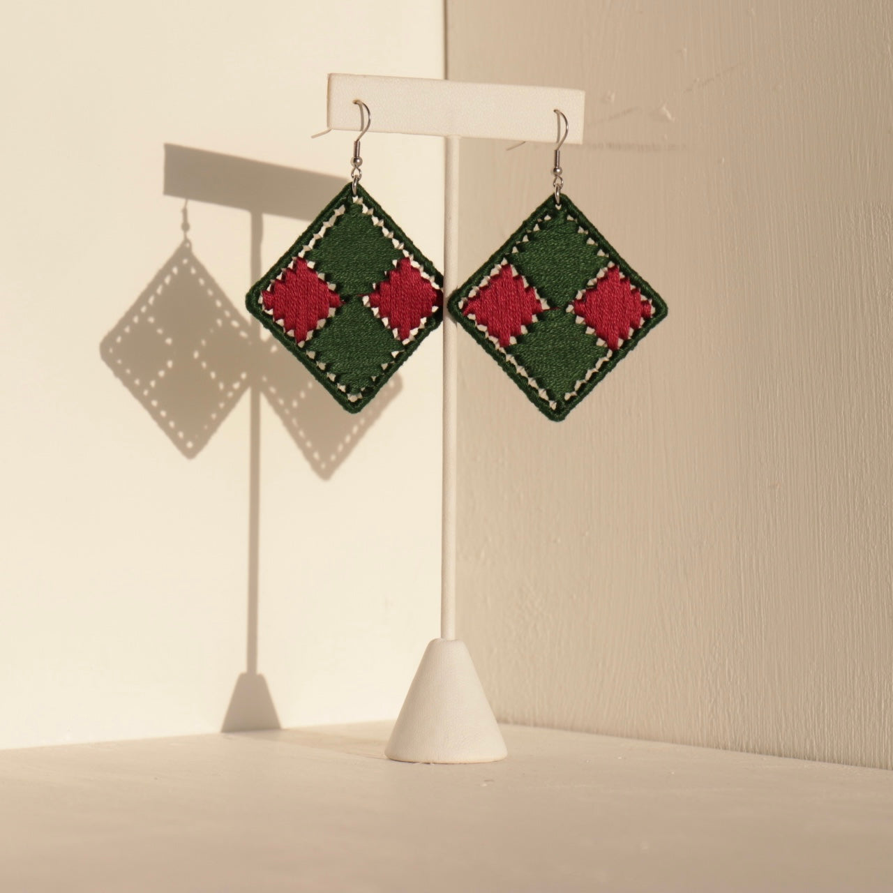 Green and pink Benni earrings displayed on a jewelry stand against a neutral backdrop