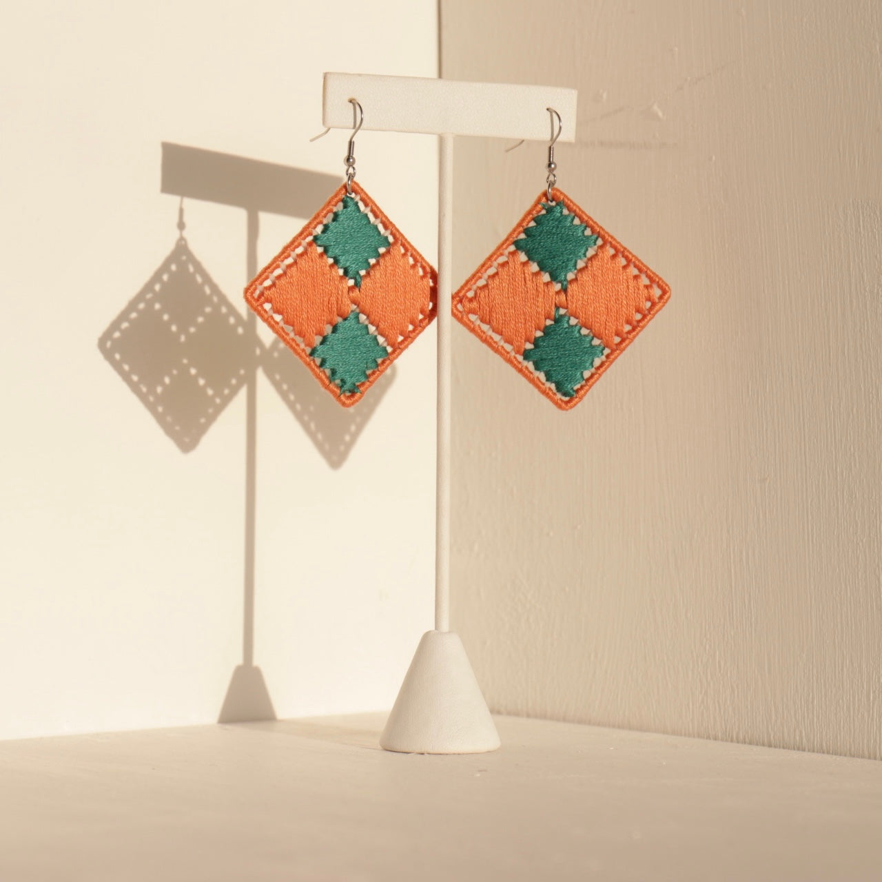 Orange and green Benni earrings showcased on a jewelry stand