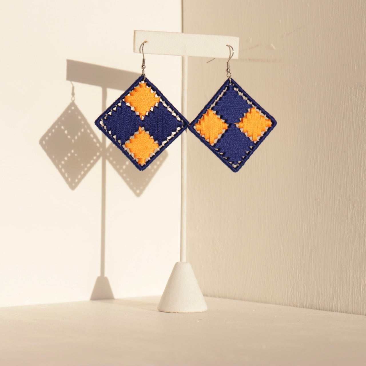 Blue and yellow Benni statement earrings displayed on a stand with soft shadows