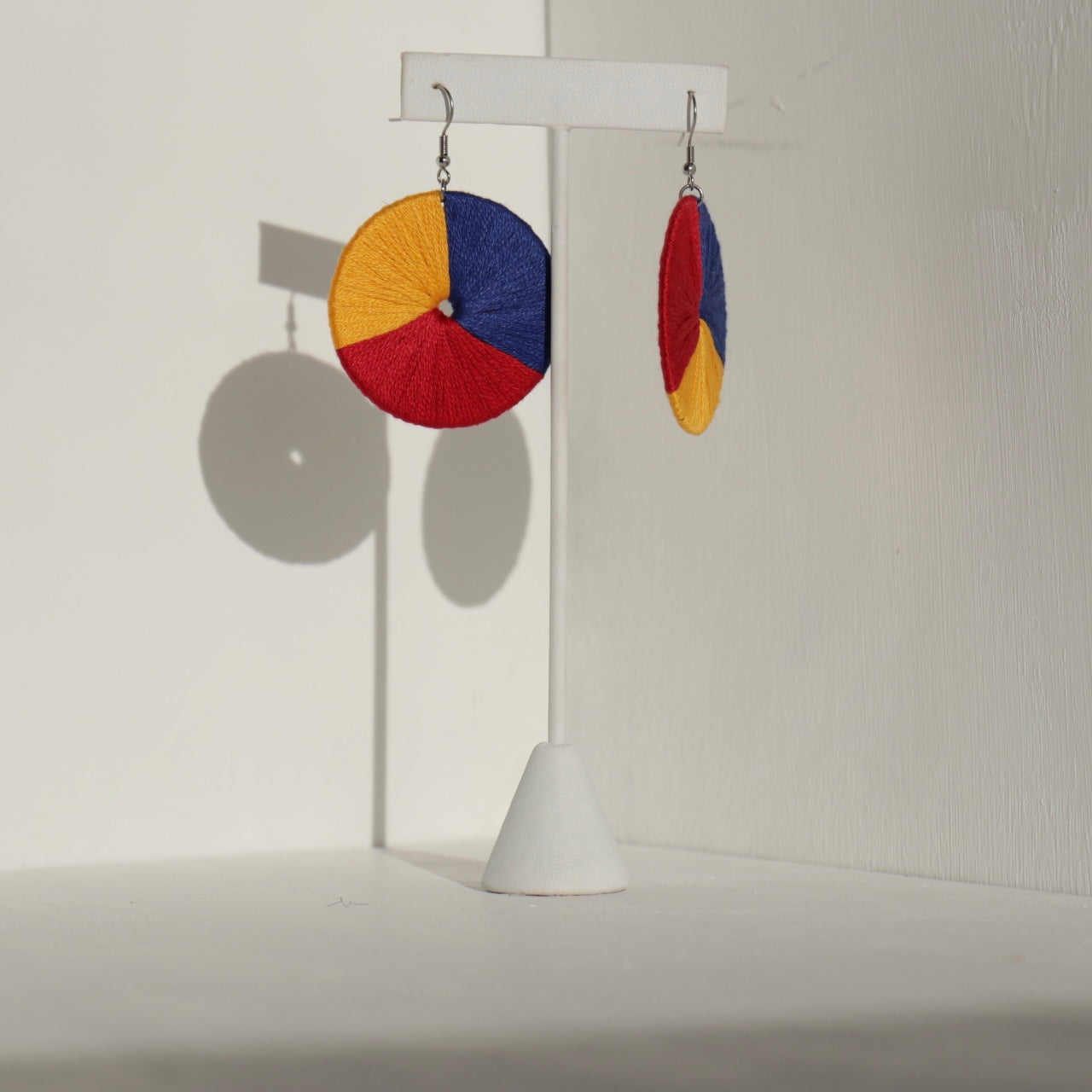 The Bode earrings featuring a striking red, yellow, and blue color scheme, hanging from a jewelry stand.