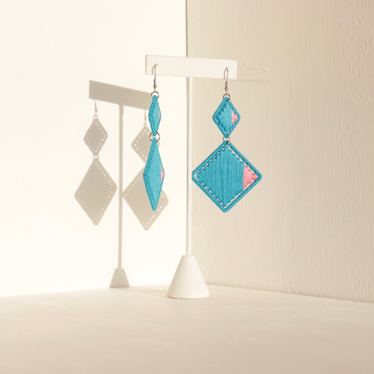 The Brisco geometric statement earrings in blue, displayed on a stand in soft lighting