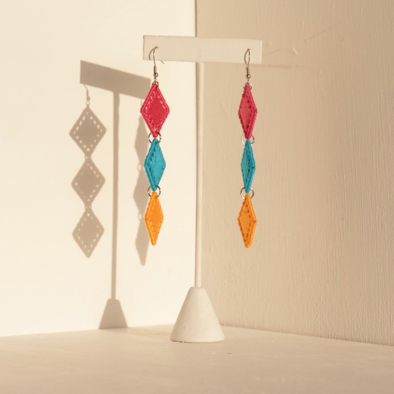 The Bunmi statement earrings in vibrant multicolor, displayed on a stand with soft shadows