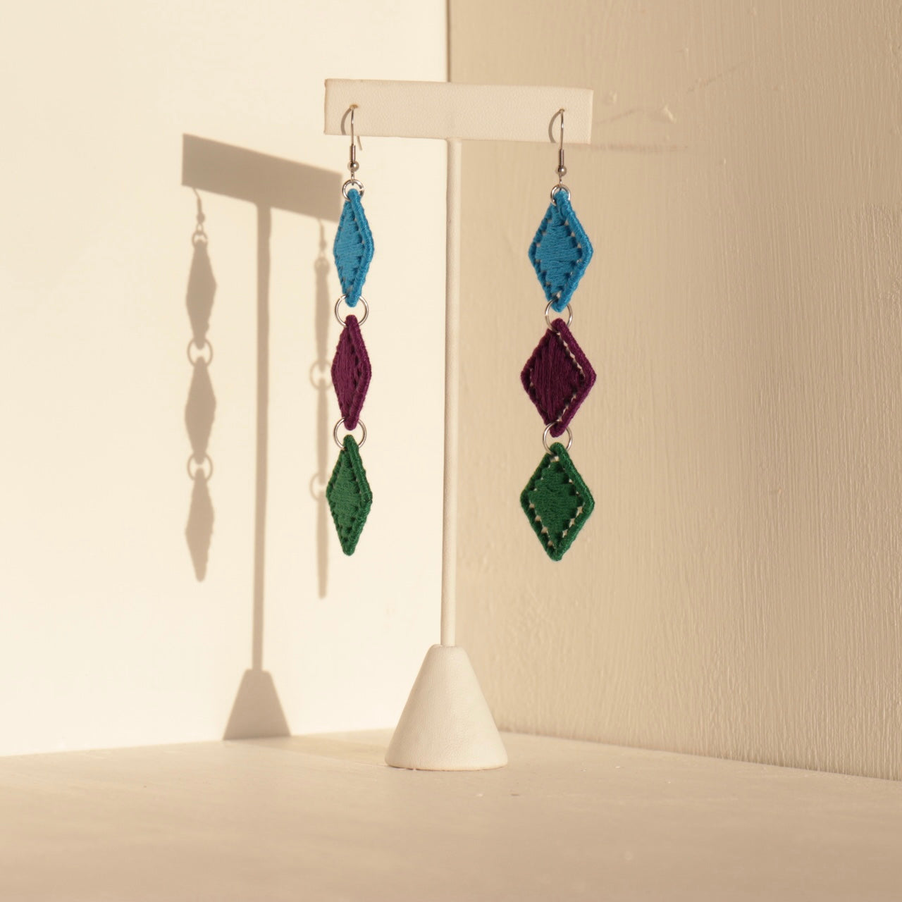 The Bunmi earrings displayed in a bold color mix, styled on a white jewelry stand
