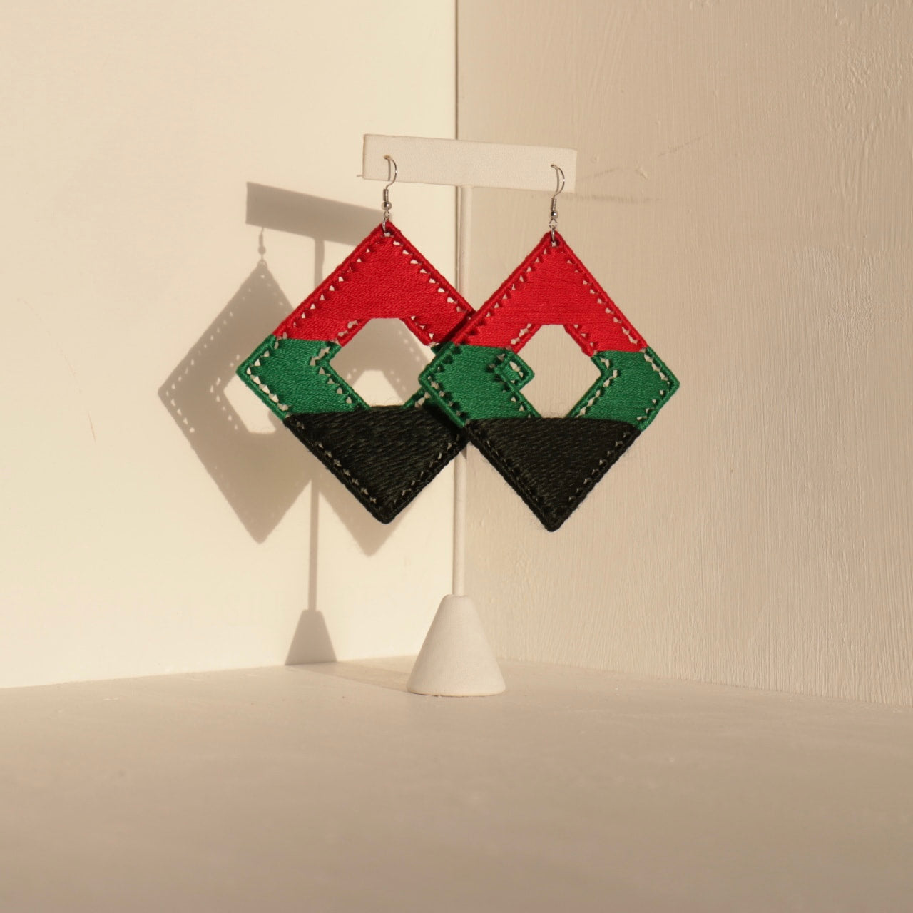 The Joel statement earrings in red, green, and black displayed on a jewelry stand