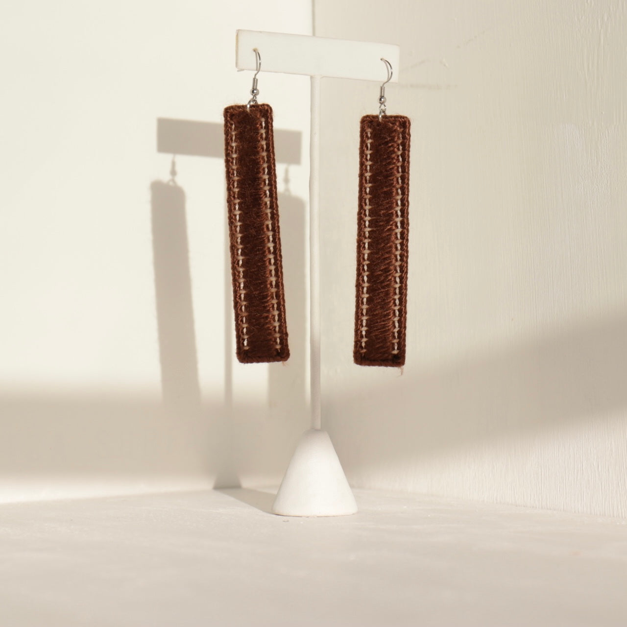 The Kevo earrings in brown displayed on a stand, minimalist yet commanding