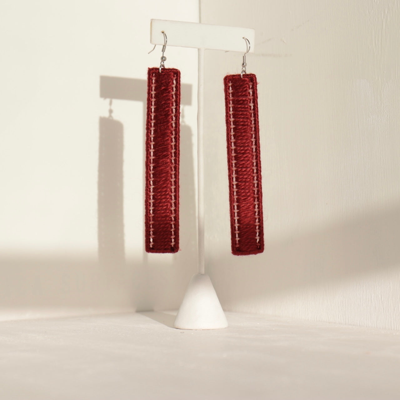 The Kevo earrings in deep red, hanging from a jewelry stand with warm lighting