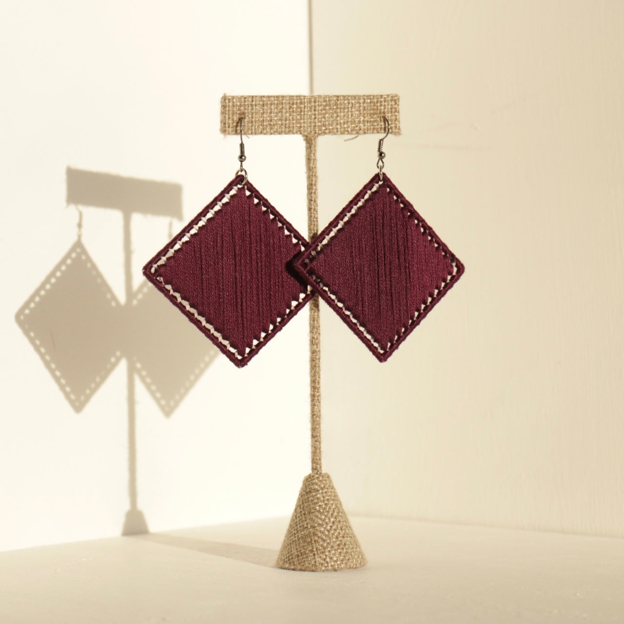 Deep red Kwame earrings displayed on a neutral stand, showcasing a bold yet minimal aesthetic