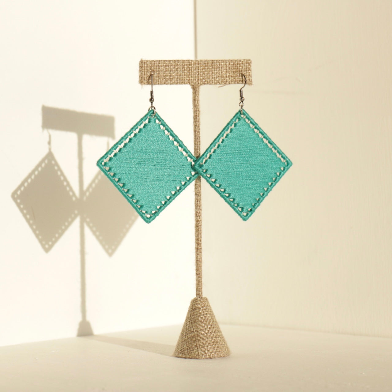 The Kwame statement earrings in vibrant green displayed on a stand with soft shadows