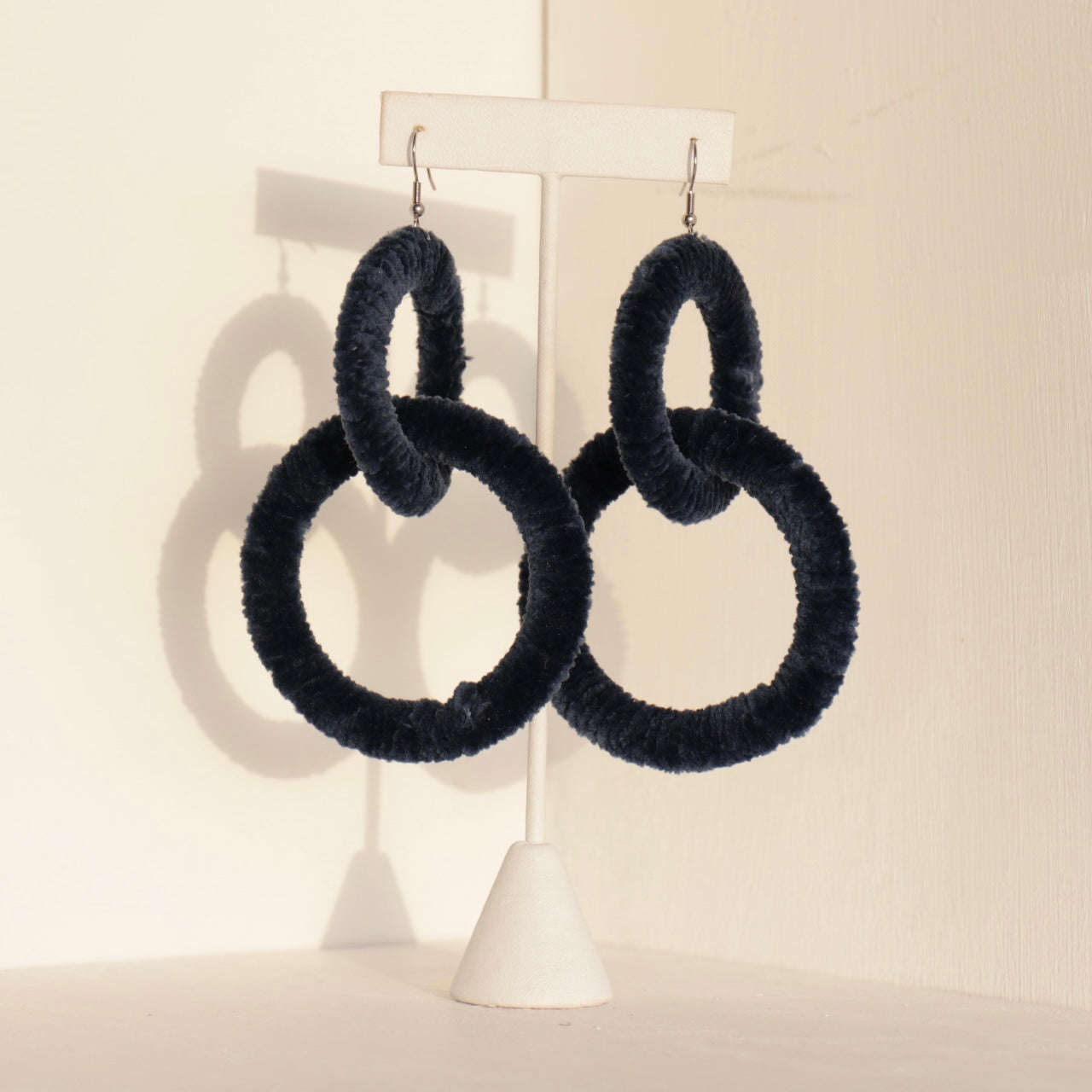 The Valente earrings in navy displayed on a stand with warm lighting