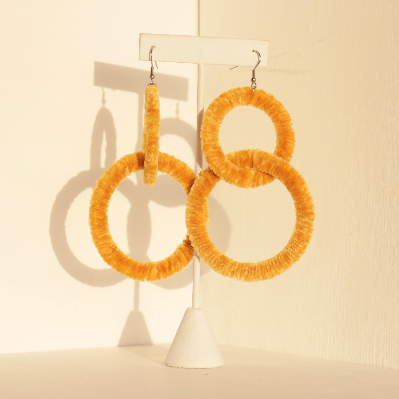 The Valente earrings in yellow displayed on a jewelry stand, highlighting their circular shape