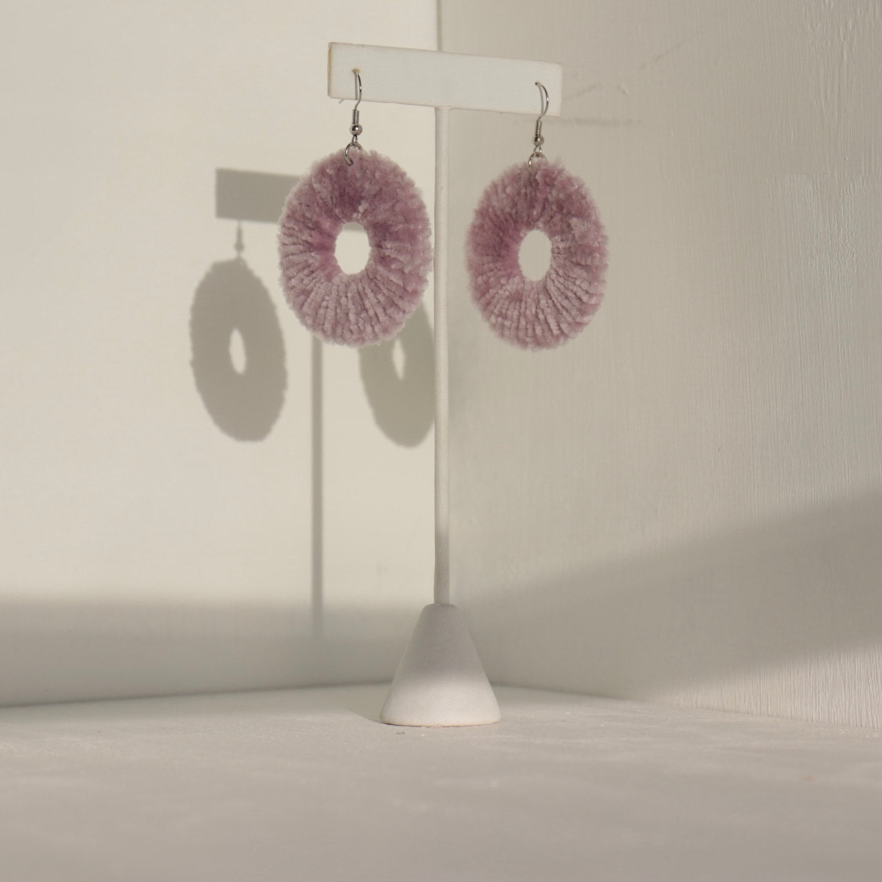 The Vinny earrings in a muted pink tone, displayed elegantly on a jewelry stand