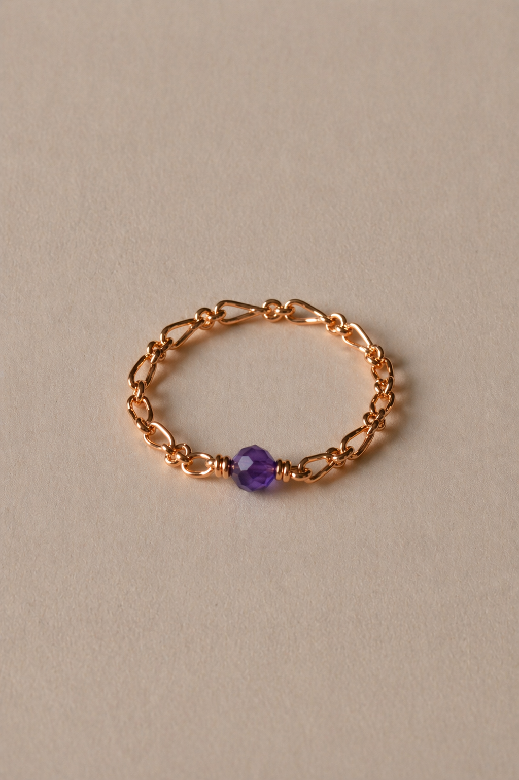 Gold chain ring with an amethyst gemstone on a beige background