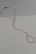 A delicate gold hand chain with textured, hammered links, laid out in a loose loop on a neutral gray surface with soft shadows.