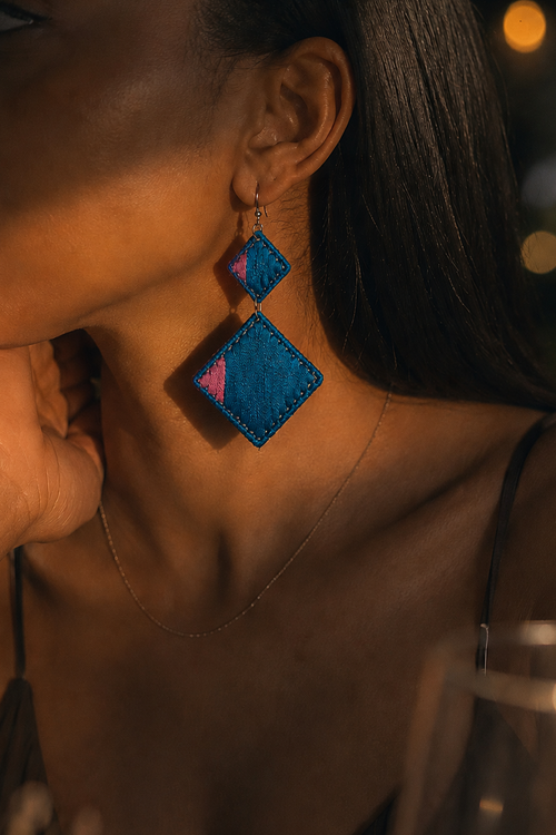 Close-up of a person wearing blue geometric earrings with a blurred background