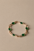 Gold chain ring with green beads on a beige background