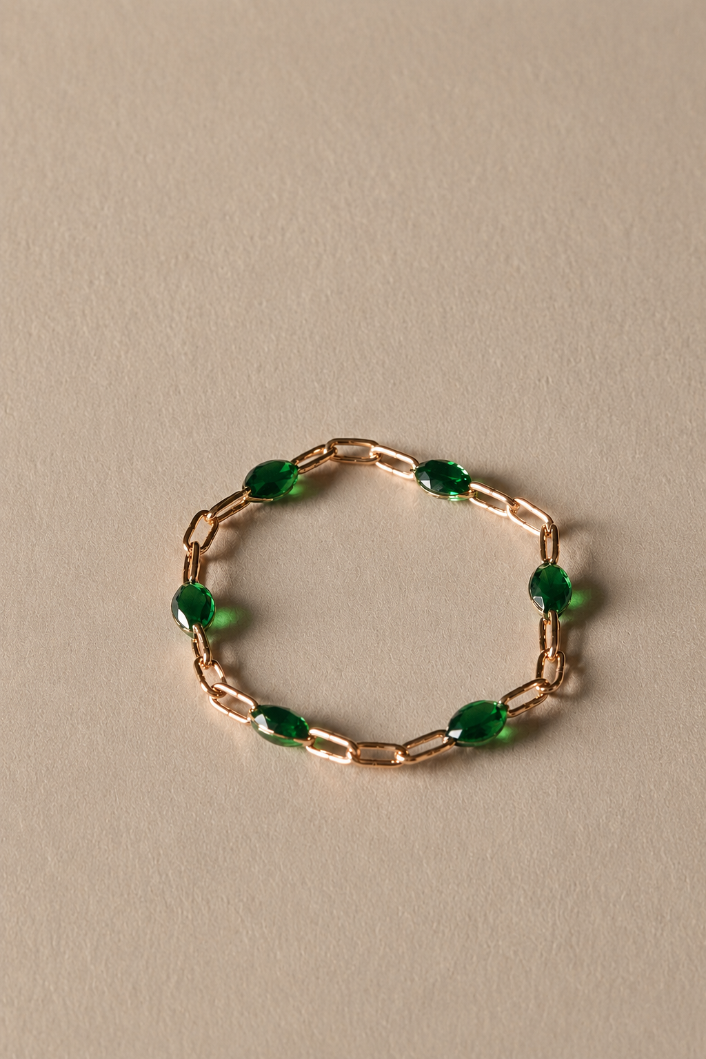 Gold chain ring with green beads on a beige background
