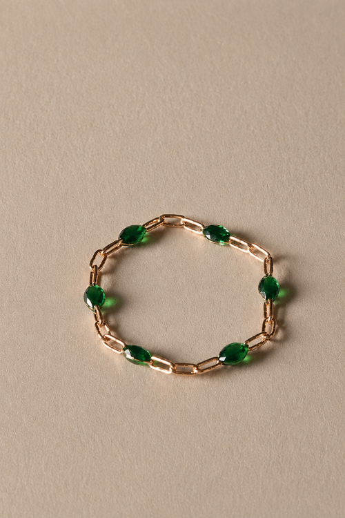 Gold chain ring with green beads on a beige background