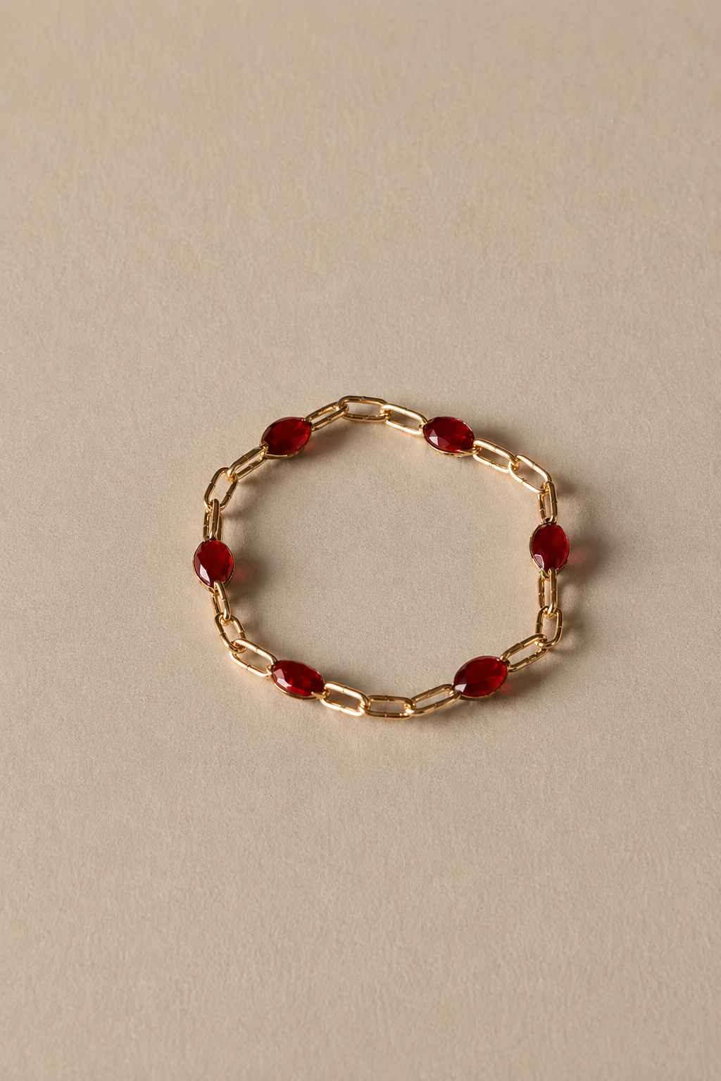 Gold chain ring with red beads on a beige background