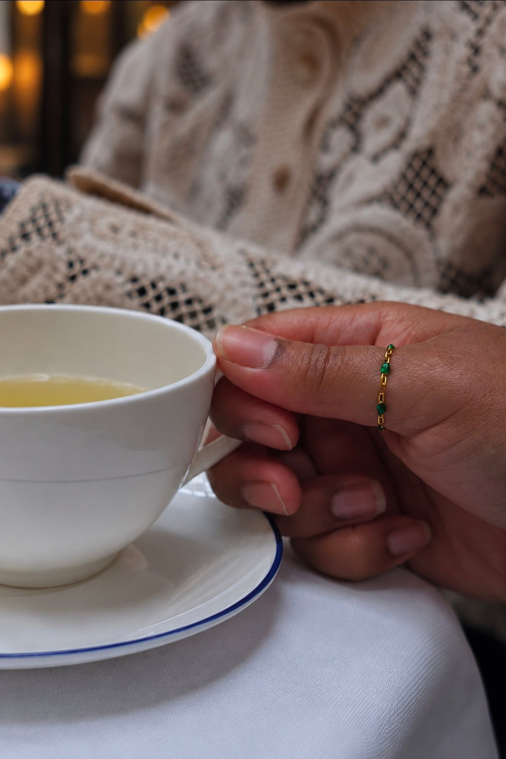 Hand holding cup of green tea work a gold chain thumb ring