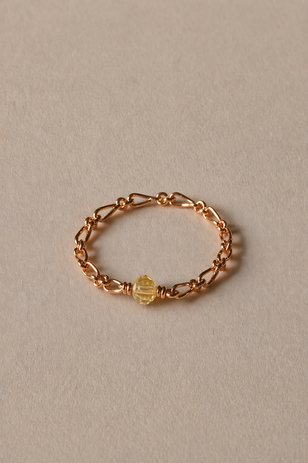 Gold chain bracelet with a citrine bead on a beige background