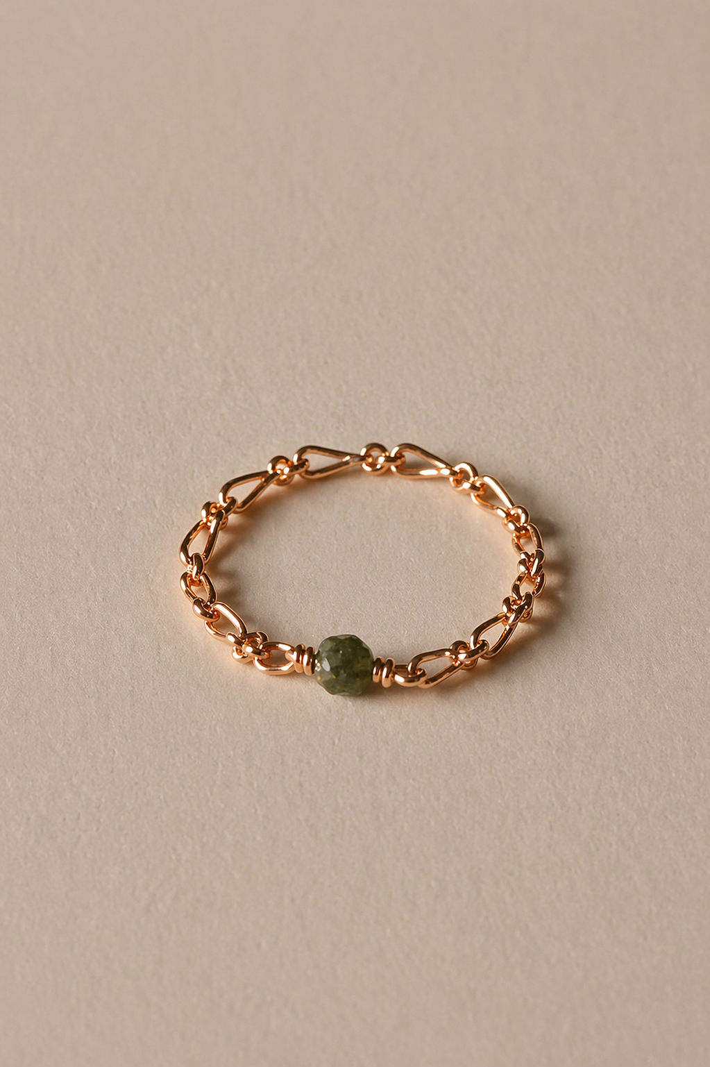 Rose gold chain ring with a emerald stone on a beige background
