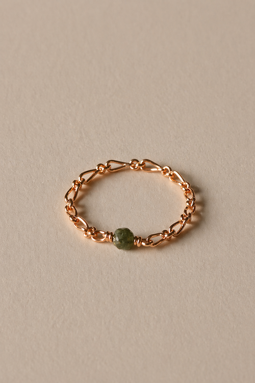 Rose gold chain ring with a emerald stone on a beige background