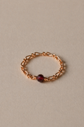 Gold chain ring with a garnet gemstone on a beige background