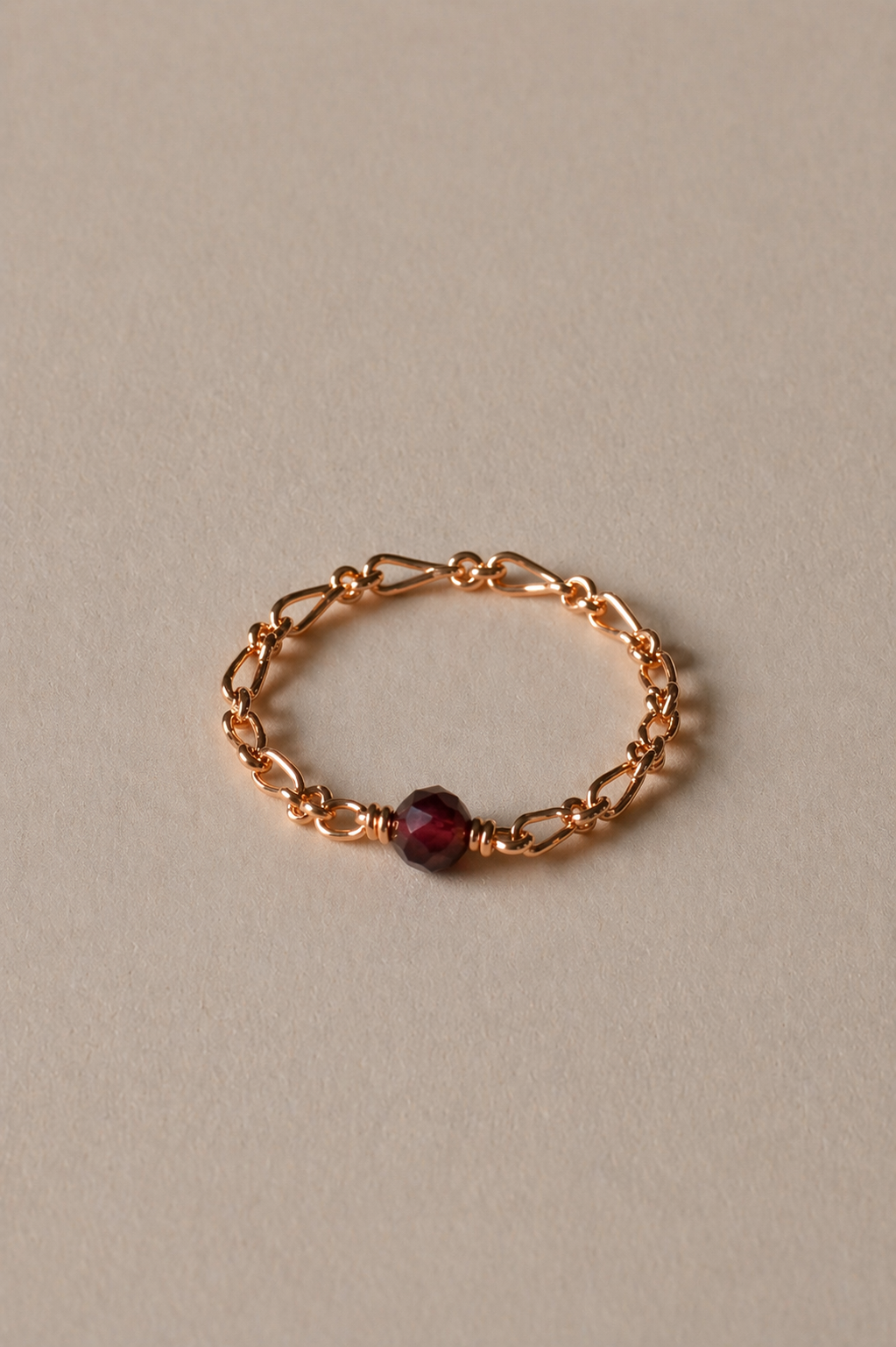 Gold chain ring with a garnet gemstone on a beige background
