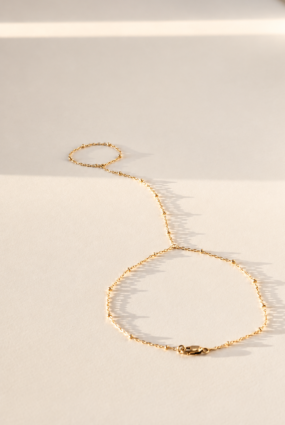 A delicate gold chain bracelet with a textured, beaded link design and a lobster clasp, displayed on a warm beige surface with soft shadows.