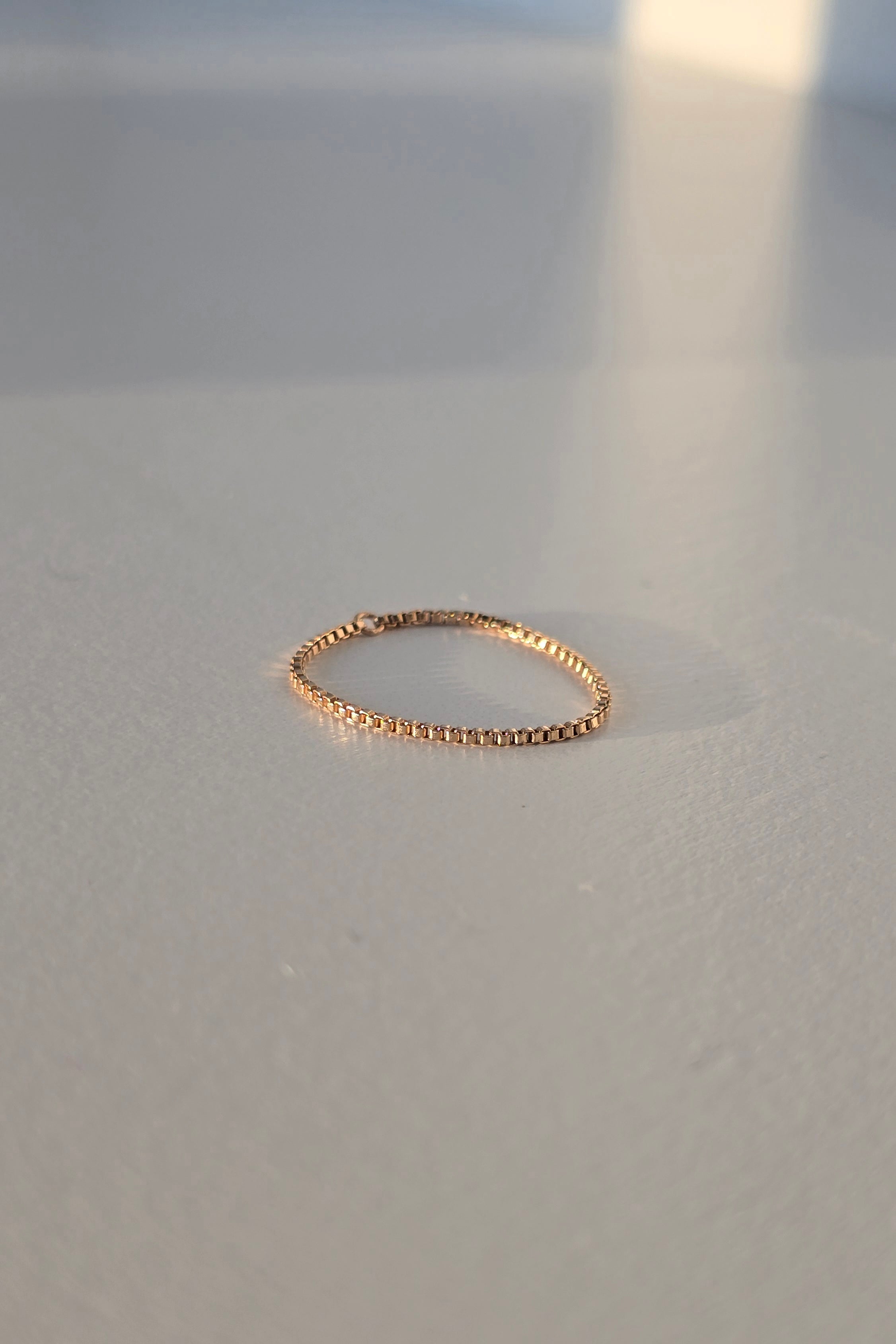 A delicate rose gold chain ring resting on a light gray surface with soft shadows.