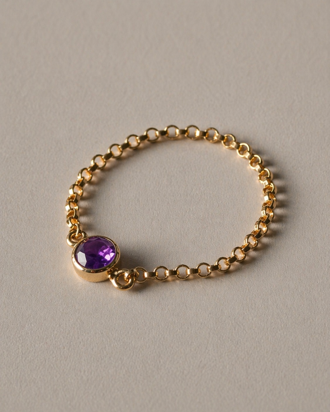 Gold chain ring with a purple gemstone on a beige background