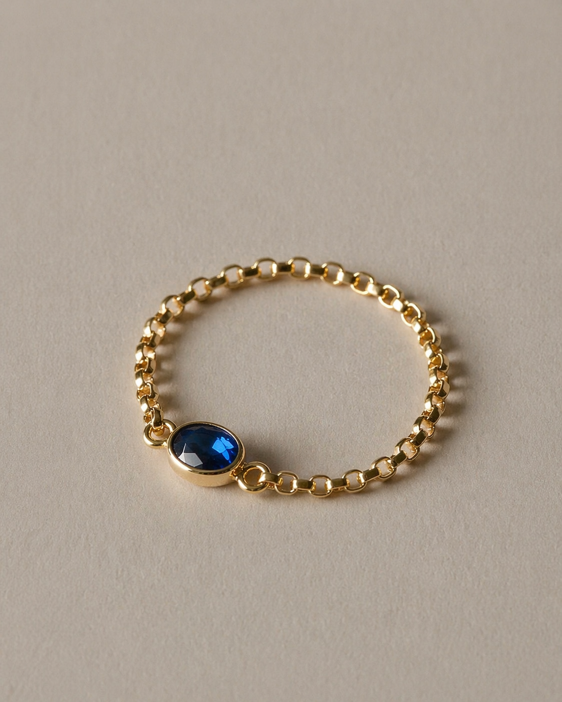 Gold chain ring with a blue gemstone on a beige background