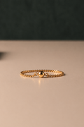 Gold chain ring with ball detail on a beige surface with a dark background