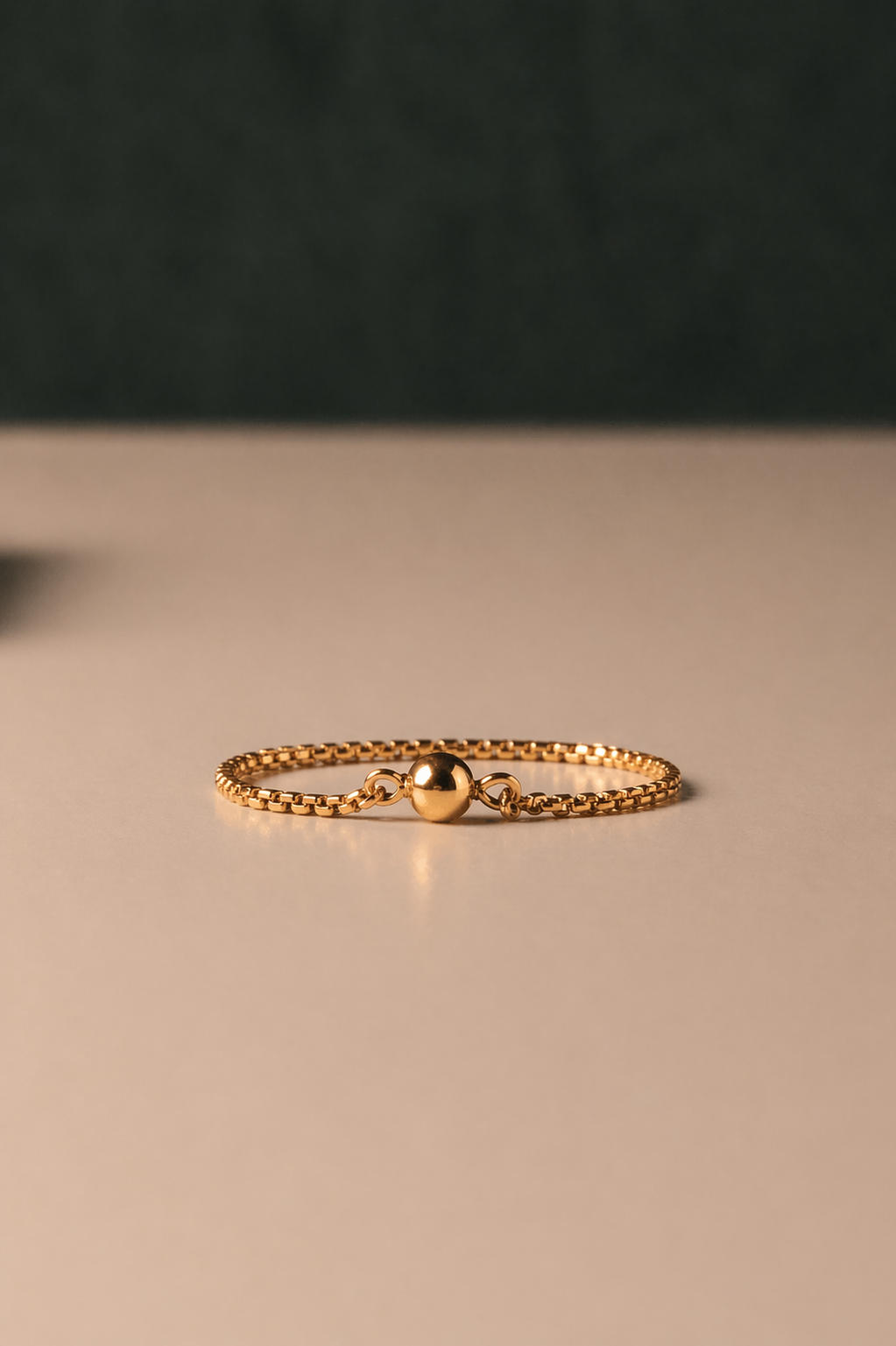 Gold chain ring with ball detail on a beige surface with a dark background