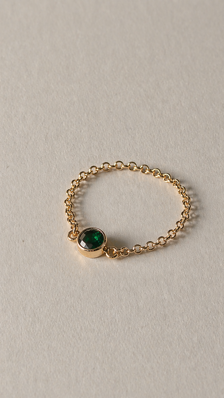 Gold ring with a green gemstone on a light beige background
