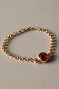 Gold chain ring with a red gemstone on a gray background