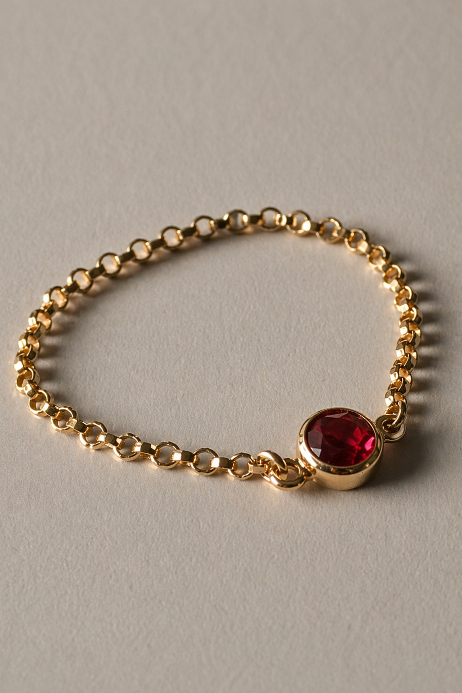 Gold chain ring with a red gemstone on a gray background