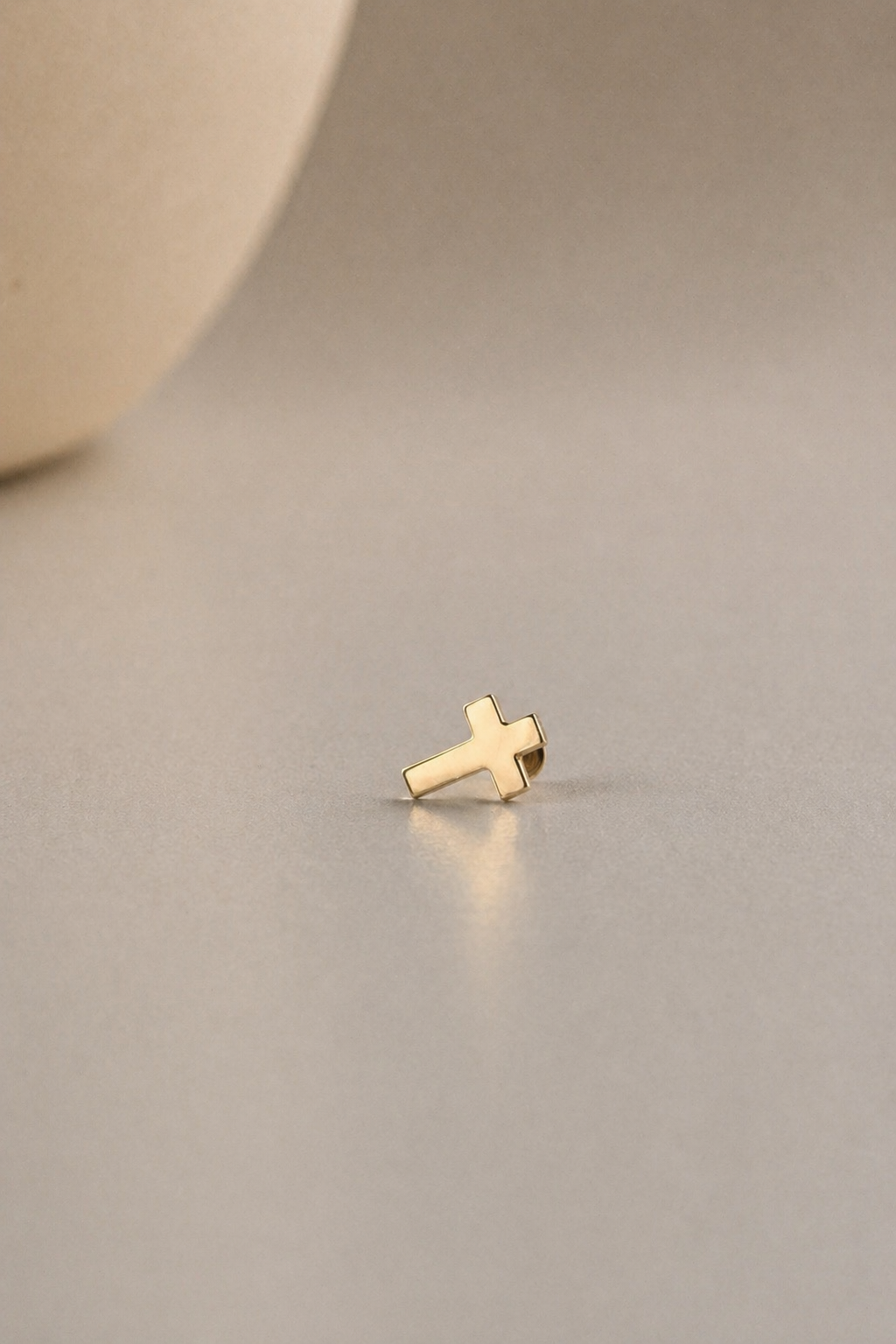 Gold cross earring on a beige background