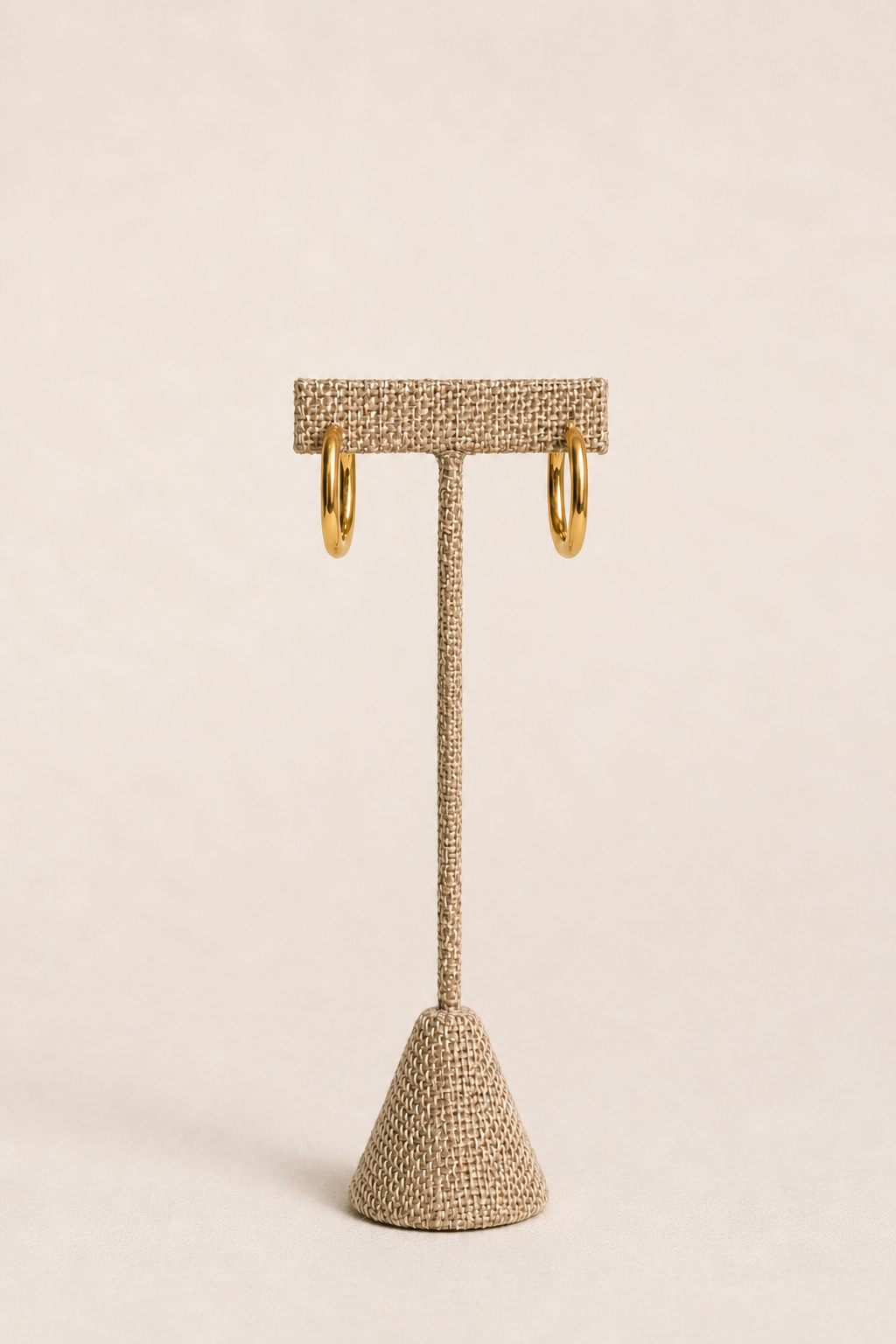 Textured earring stand with gold hoop earrings on a beige background