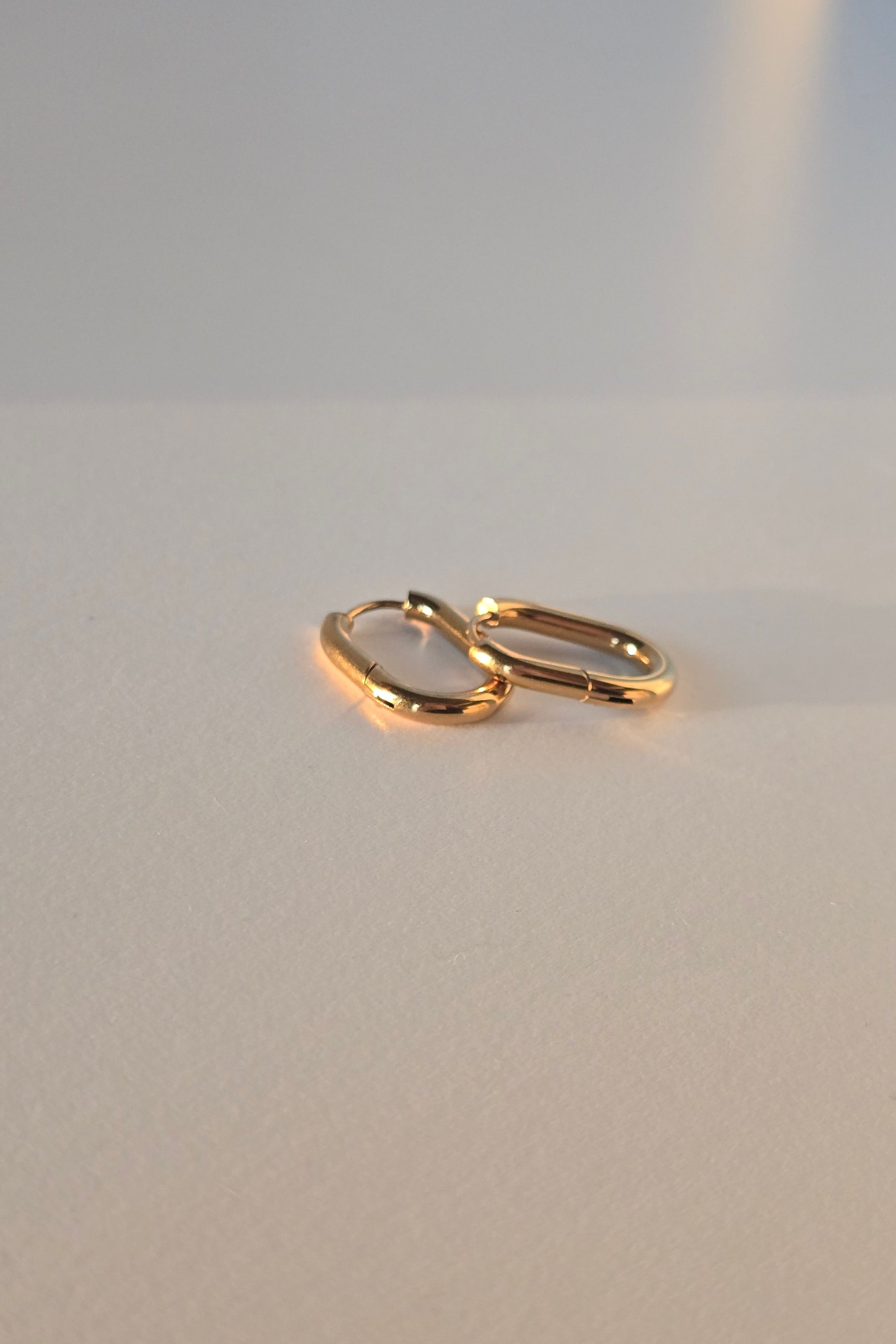 A pair of gold hoop earrings on a plain light gray surface.