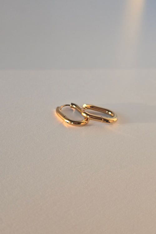 A pair of gold hoop earrings on a plain light gray surface.