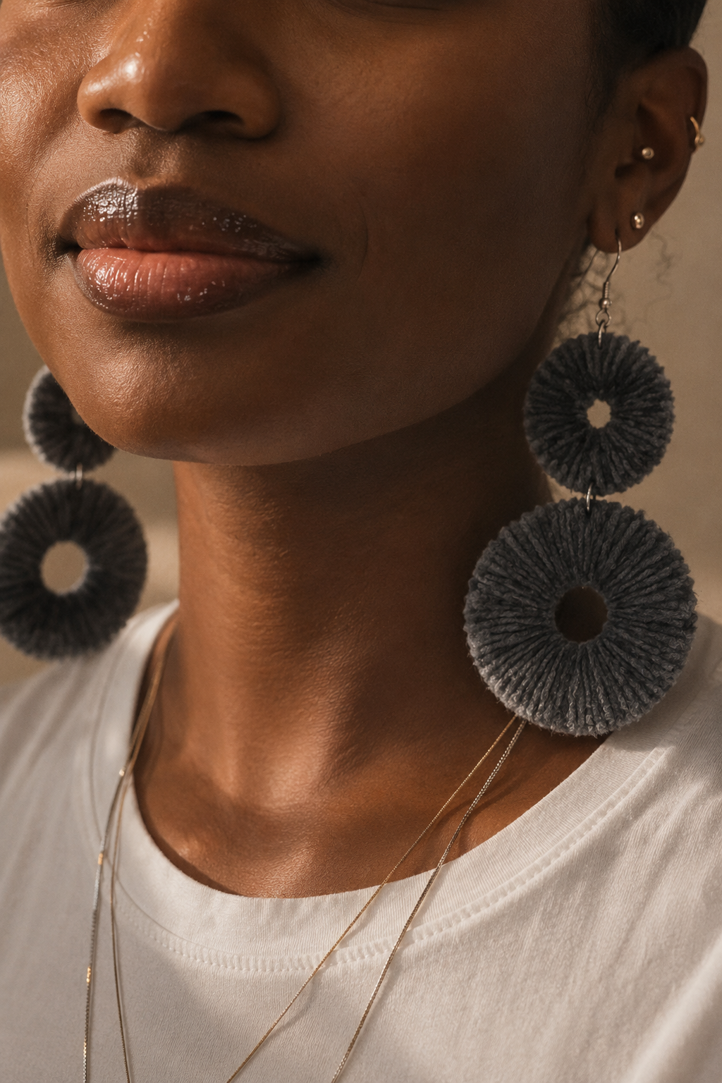 Close-up of a woman wearing large, dark gray velvet earrings with a neutral background