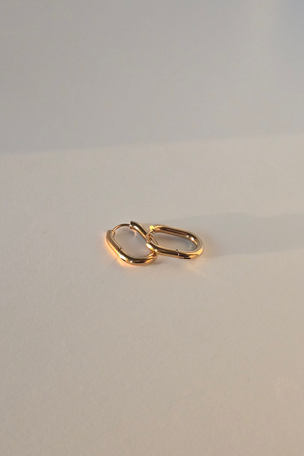 Gold huggie hoop earrings on a beige textured surface
