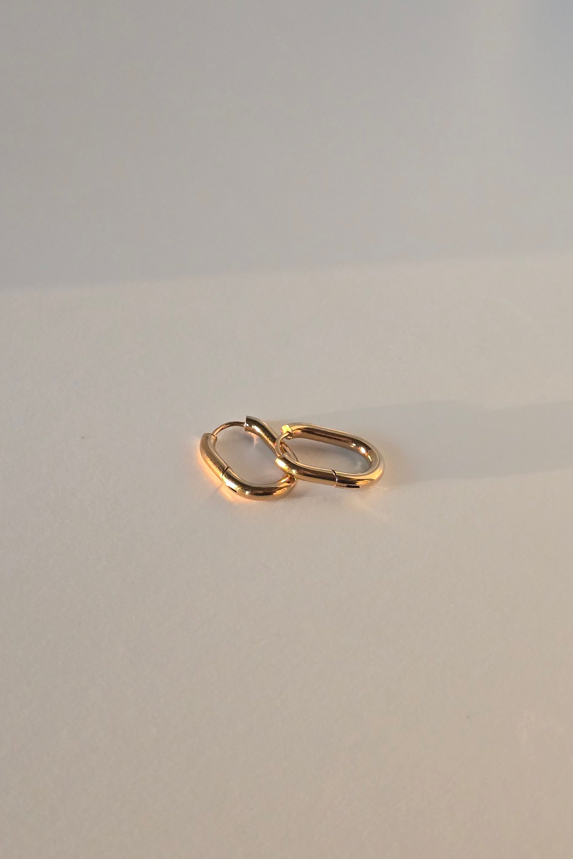 Gold huggie hoop earrings on a beige textured surface