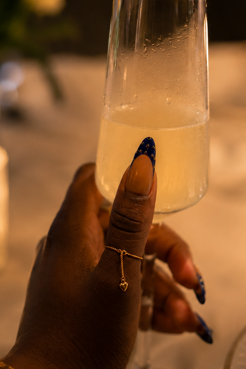 Hand holding a glass of champagne with candles and flowers in the background