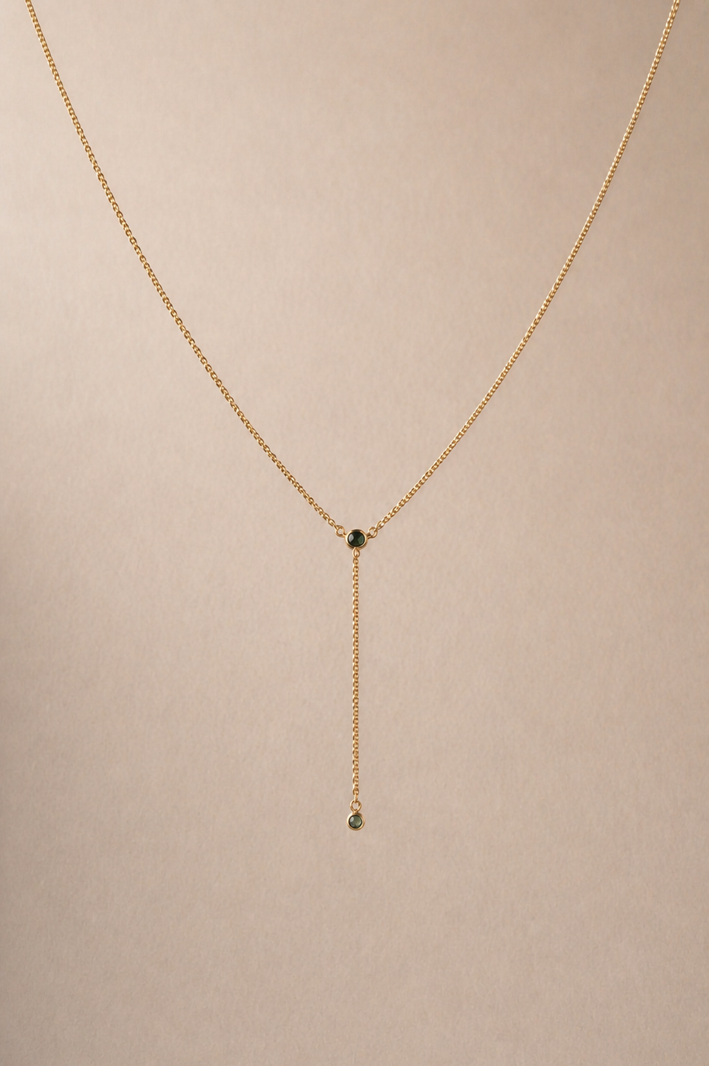 Gold necklace with a small green gemstone on a beige background