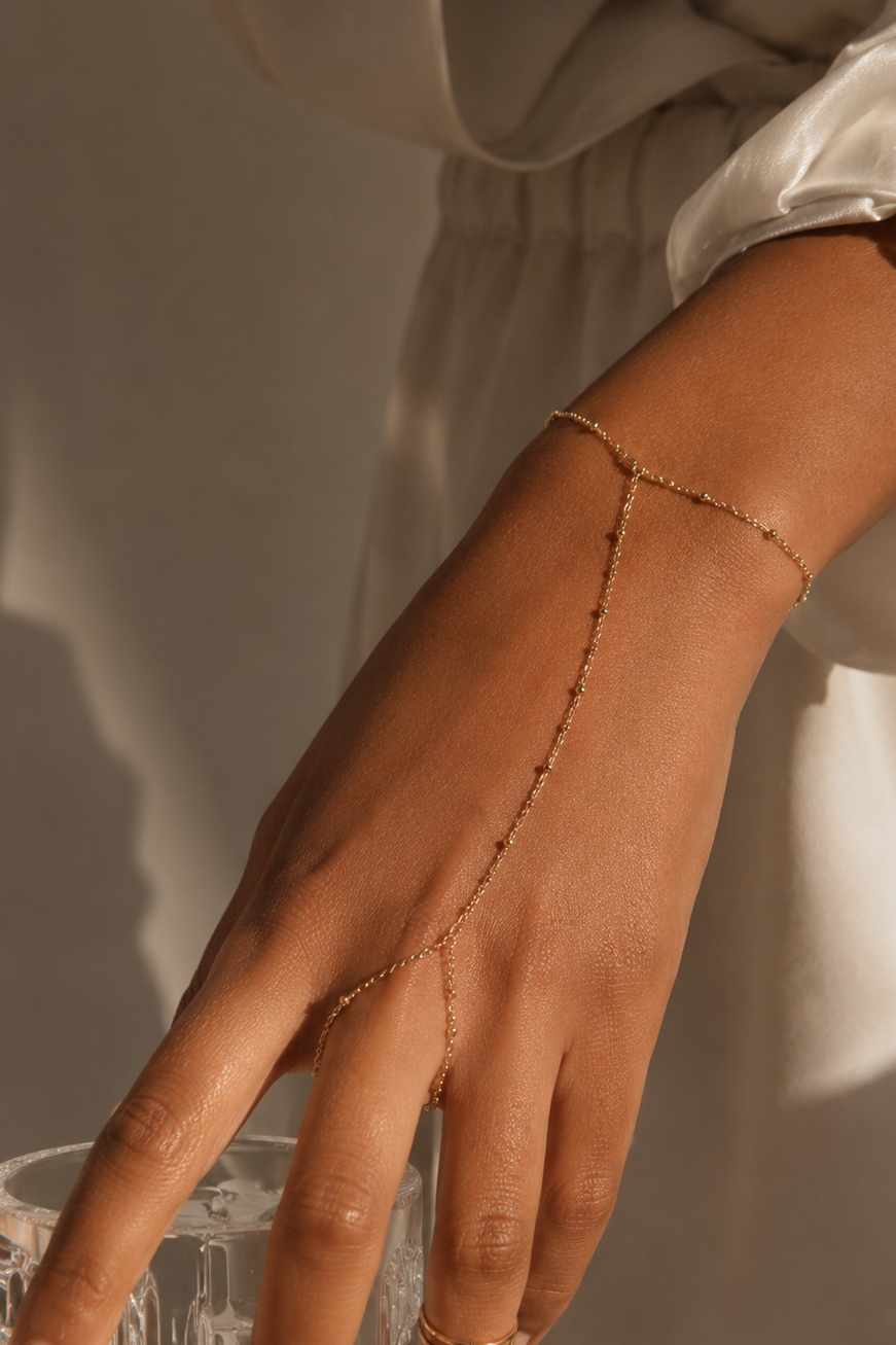 Hand wearing a delicate gold hand chain bracelet with a blurred background