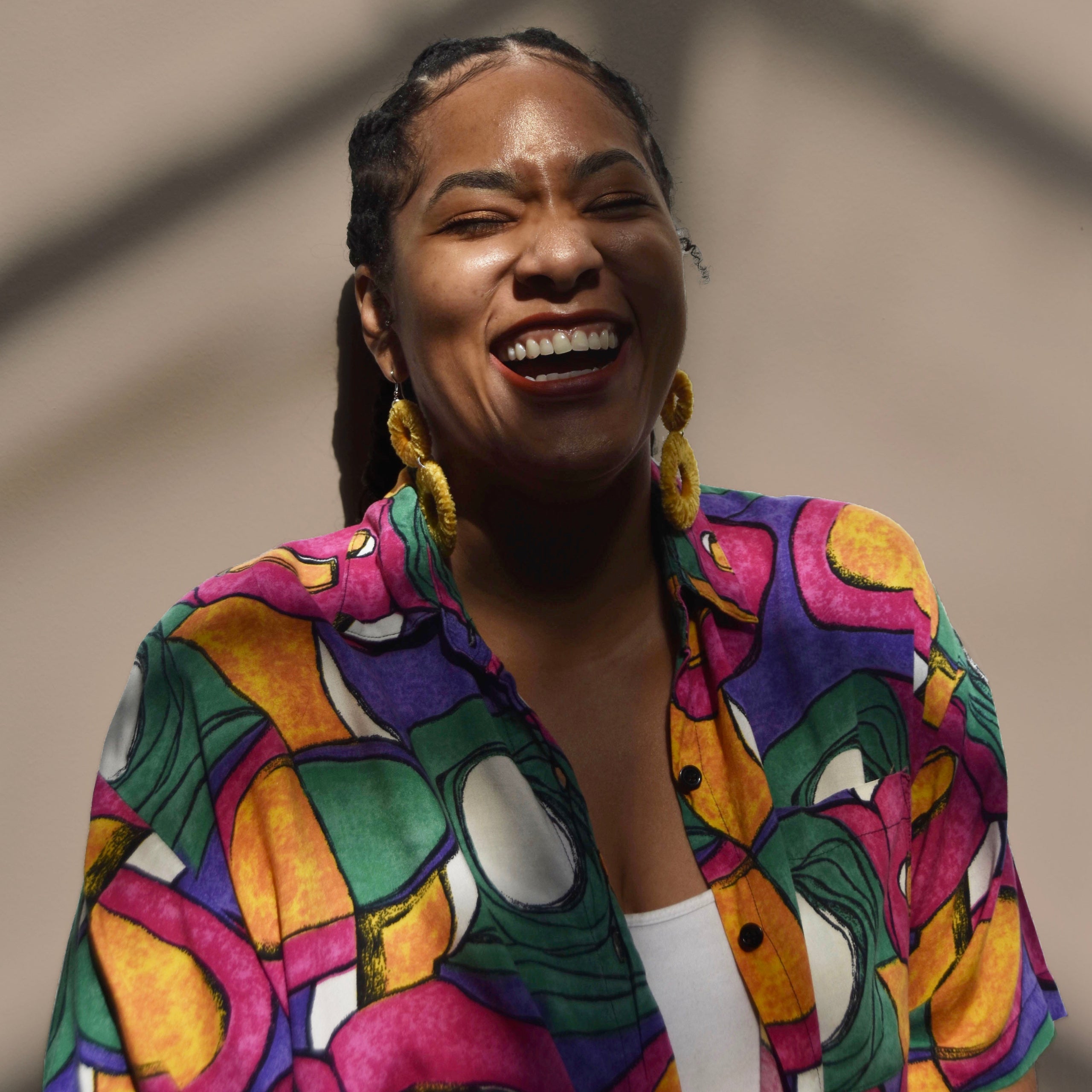 Woman smiling wearing a colorful shirt and statement earrings